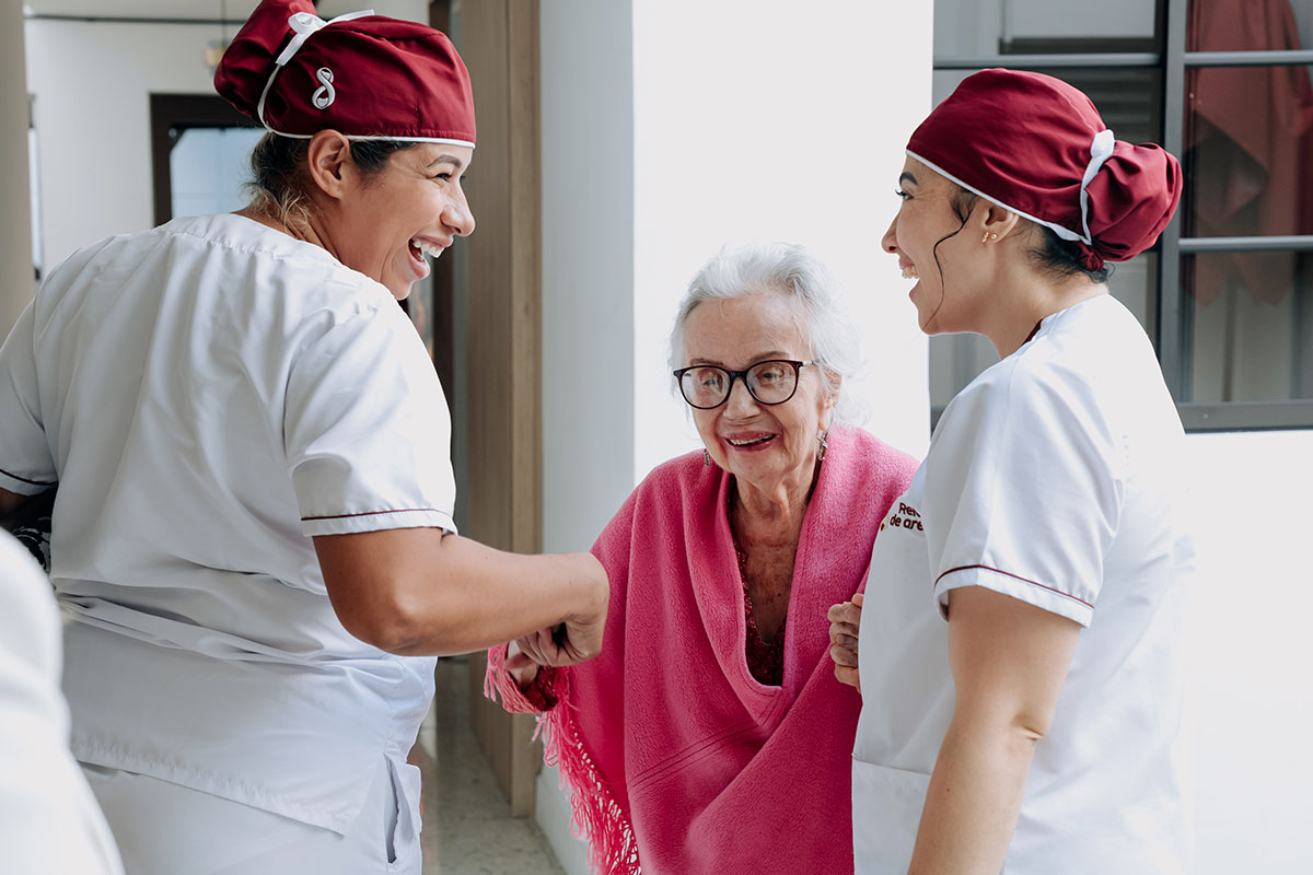 Cuidadoras conversan con una residente sonriente