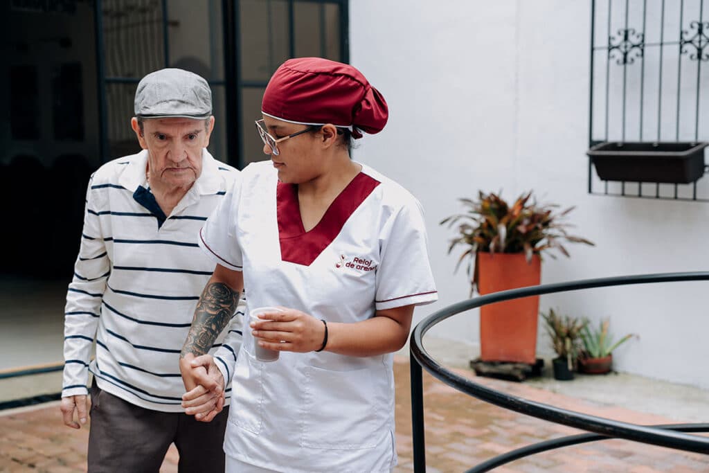 Cuidadora acompaña a un adulto mayor a caminar en el patio