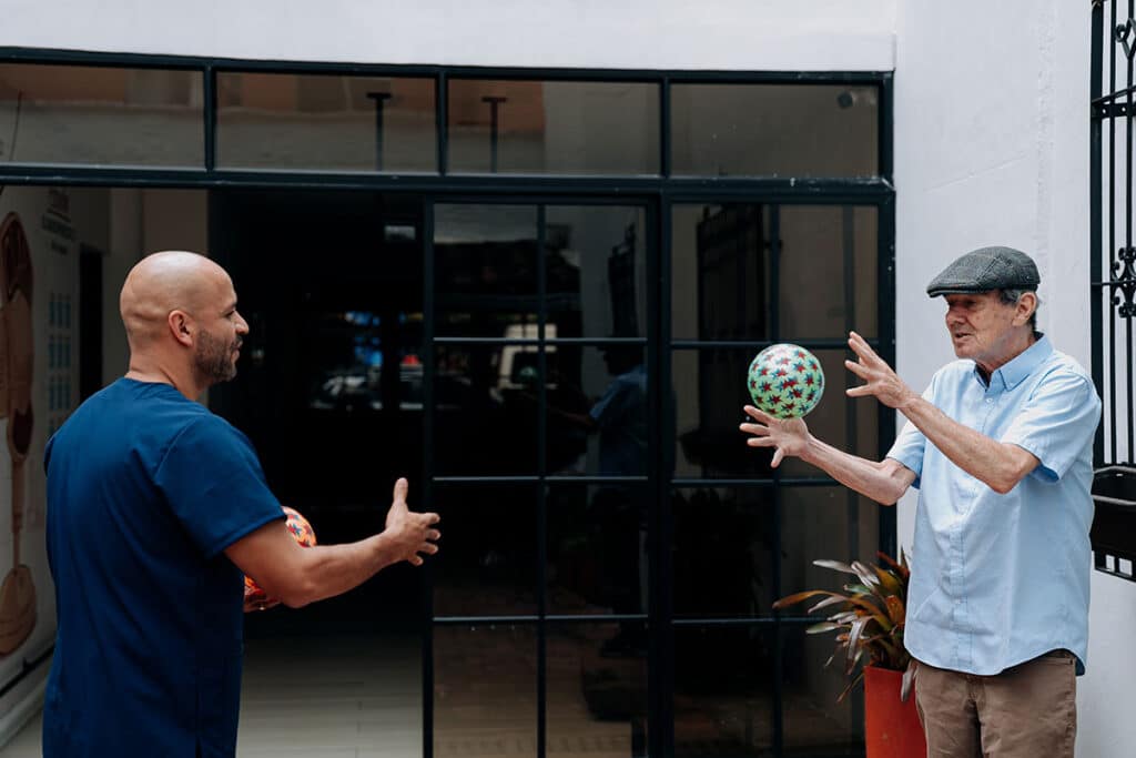Fisioterapeuta lanza una pelota a un adulto mayor durante la terapia